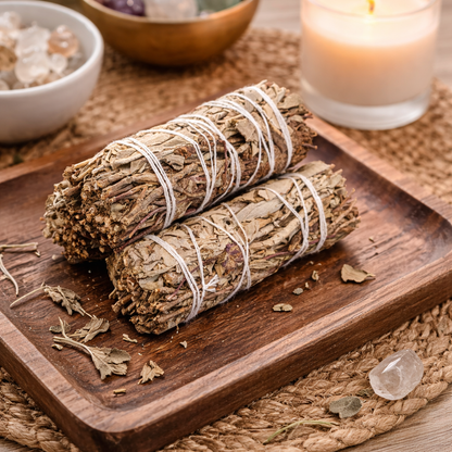 Two bundles of sage on a wooden tray with a candle in the background.