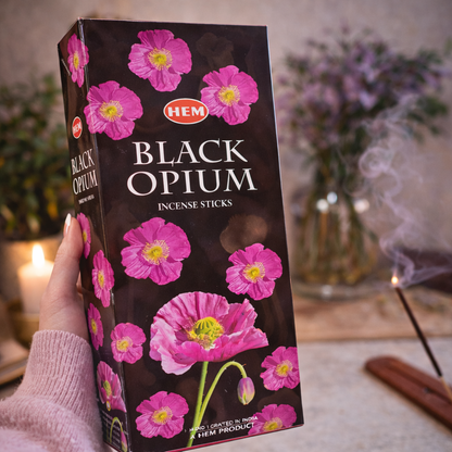 Hand holding HEM Black Opium incense sticks box beside burning incense
