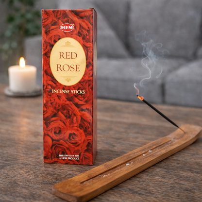 HEM Red Rose incense sticks box with burning incense on a wooden table beside a candle