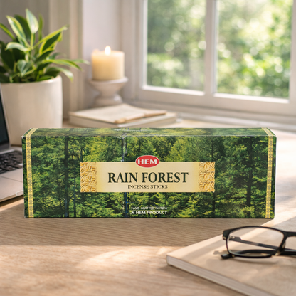 HEM Rain Forest incense sticks box on a desk by a window with a candle and plant