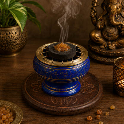 Lifestyle image of light blue and gold incense burner with brass screen, burning resin incense, and carved wooden coaster.
