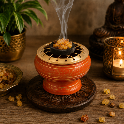 Lifestyle image of orange and gold incense burner with brass screen, burning resin incense, and carved wooden coaster.