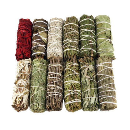 A variety of sage smudge sticks arranged side by side, each bundle wrapped in string. The colors of the herbs vary, indicating different types of sage and other herbs included in the set.